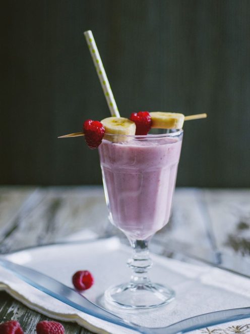 Frappè di banane e lamponi guarnito con fettine di banana e lamponi freschi su spiedino