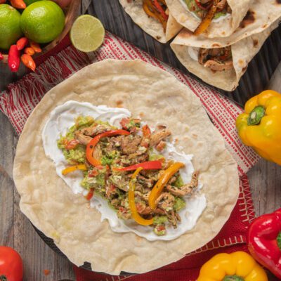 Fajitas con pollo grigliato, peperoni saltati, guacamole e panna acida su tortilla aperta