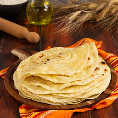 Piadine sottili impilate con macchie di cottura dorate, servite su tagliere