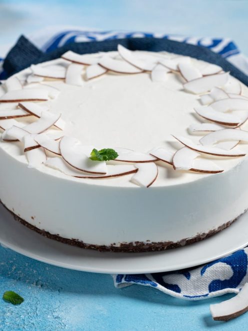 Cheesecake al cocco con scaglie di cocco fresco disposte a corona e una fogliolina di menta al centro