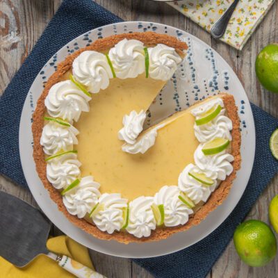 Key lime pie con base di biscotto, crema al lime e ciuffi di panna, una fetta già servita