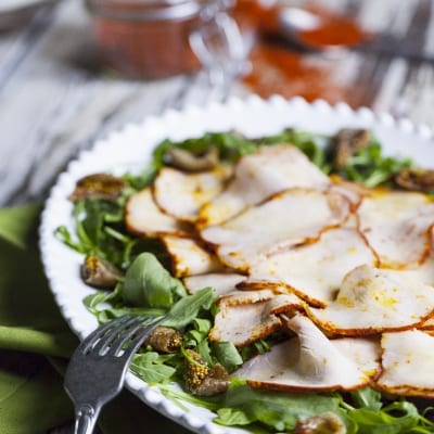 Lonza di maiale affettata su letto di rucola con fichi secchi e crosta speziata