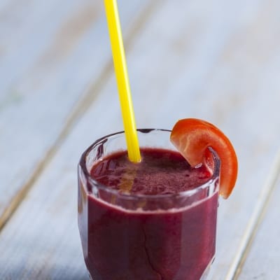 Succo di carota, mela, pomodoro e sedano con cannuccia gialla e fetta di pomodoro sul bordo