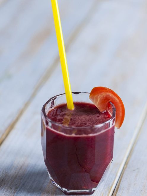Succo di carota, mela, pomodoro e sedano con cannuccia gialla e fetta di pomodoro sul bordo