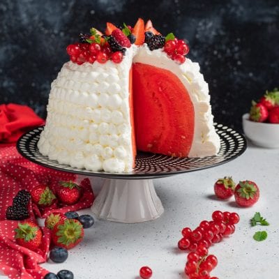 Zuccotto di anguria affettato con interno rosso, rivestito di panna e guarnito con fragole, ribes e more