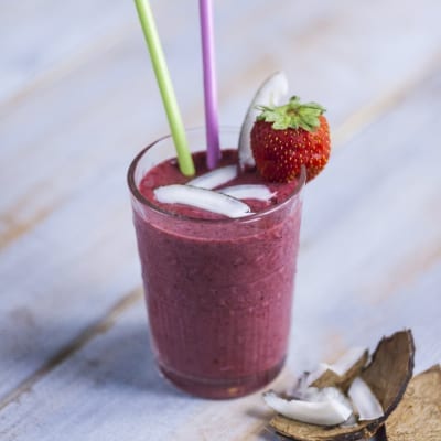 Frullato di frutti di bosco con cubetti di ghiaccio, cannucce colorate e una fragola fresca sul bordo