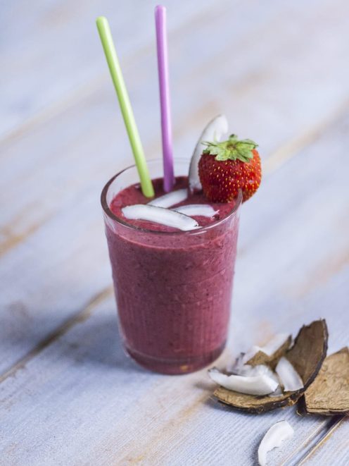 Frullato di frutti di bosco con cubetti di ghiaccio, cannucce colorate e una fragola fresca sul bordo