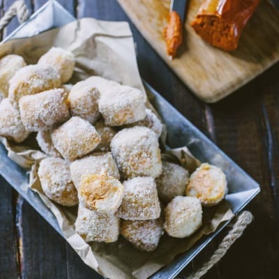 Pasta lievitata fritta spolverata di zucchero a velo, servita in abbondanza con uno spaccato che rivela il ripieno dorato