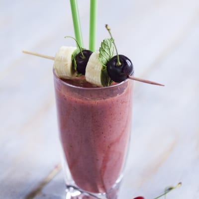 Smoothie di ciliegie, banana e succo di melograno guarnito con spiedino di frutta fresca e foglie di menta