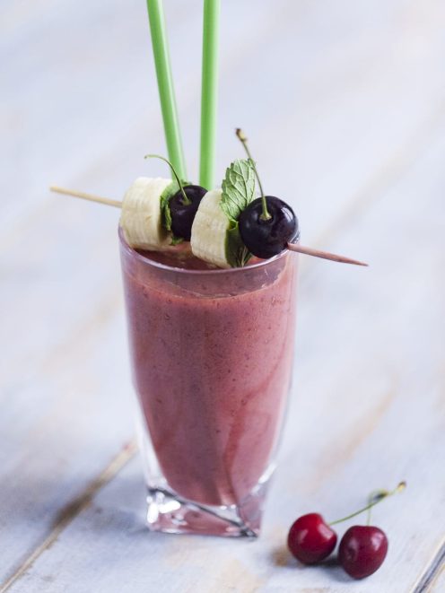 Smoothie di ciliegie, banana e succo di melograno guarnito con spiedino di frutta fresca e foglie di menta