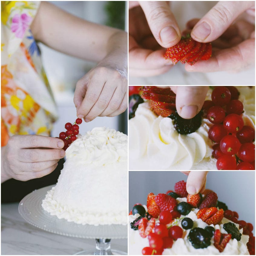 Mani che decorano uno zuccotto panna con fragole, ribes rossi e frutti di bosco freschi