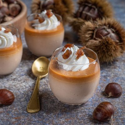 Panna cotta alle castagne in bicchiere, con strato di caramello e ciuffo di panna montata guarnito di castagne caramellate