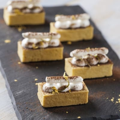 Tartellette al marron glacé con ciuffi di panna e cacao in polvere, servite in fila