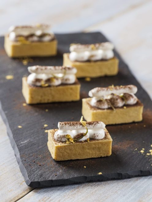 Tartellette al marron glacé con ciuffi di panna e cacao in polvere, servite in fila