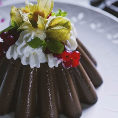 Budino al cioccolato sformato, guarnito con panna montata, ribes rosso e alchechengi