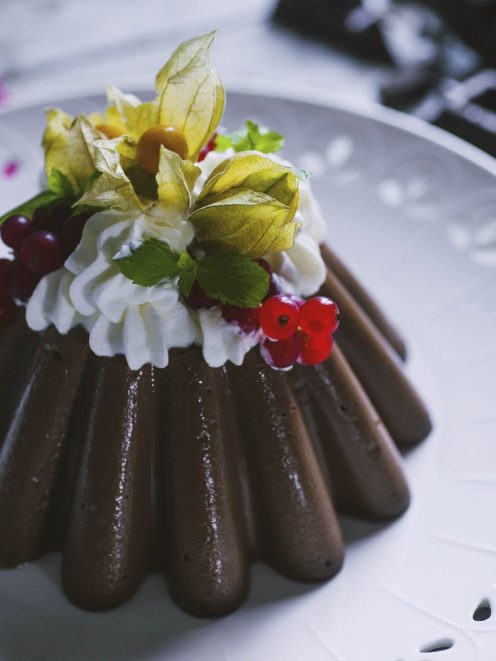 Budino al cioccolato sformato, guarnito con panna montata, ribes rosso e alchechengi