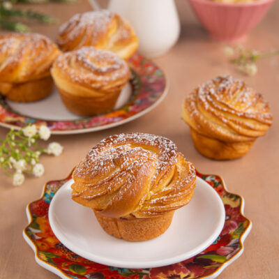 Cruffin dorato a spirale con zucchero a velo, servito su piattino
