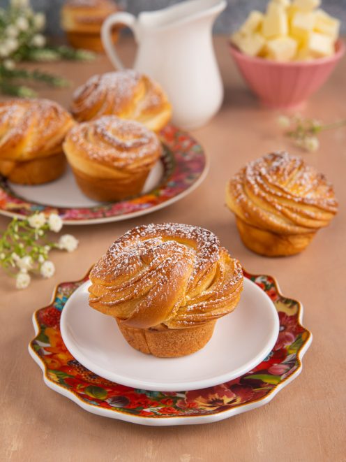 Cruffin dorato a spirale con zucchero a velo, servito su piattino