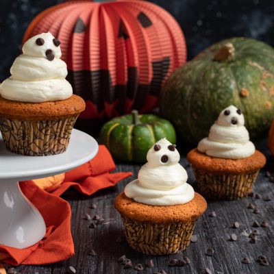 Cupcake di zucca decorati con frosting a forma di fantasma e gocce di cioccolato per Halloween