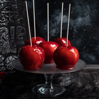 Mele caramellate con glassa rossa lucida e bastoncino, servite su alzata