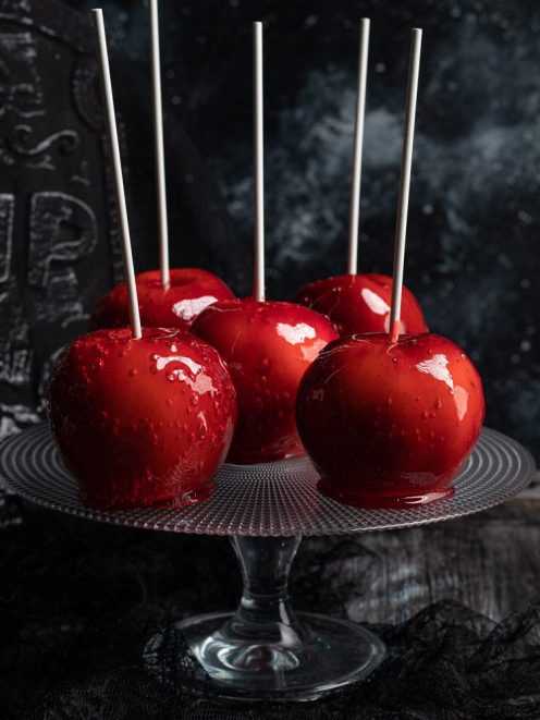 Mele caramellate con glassa rossa lucida e bastoncino, servite su alzata