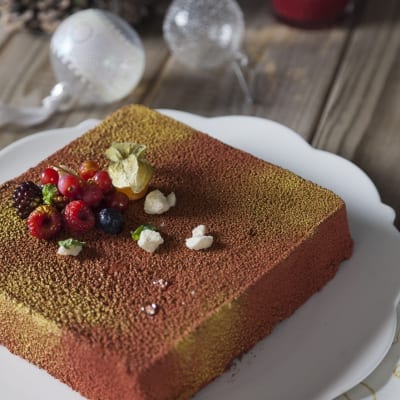 Mousse al cioccolato con biscotti rivestita di velluto cacao e oro, guarnita con frutti di bosco e physalis