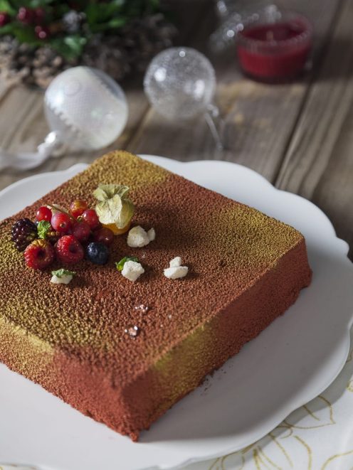 Mousse al cioccolato con biscotti rivestita di velluto cacao e oro, guarnita con frutti di bosco e physalis