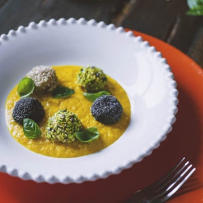 Polpette di gamberi impanate con semi diversi su vellutata dorata, guarnite con foglie di basilico