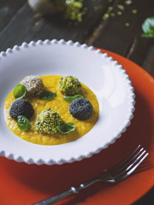 Polpette di gamberi impanate con semi diversi su vellutata dorata, guarnite con foglie di basilico