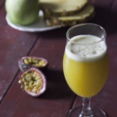 Succo di ananas, mela verde e passion fruit con schiuma in calice, affiancato da frutta fresca tagliata