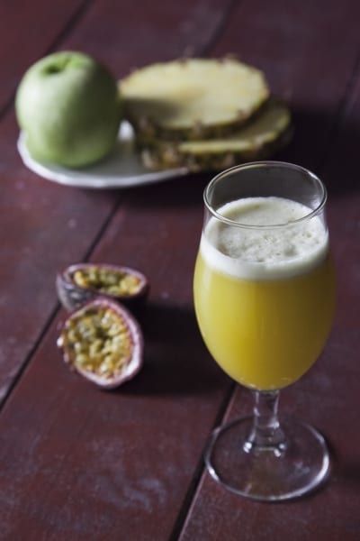 Succo di ananas, mela verde e passion fruit con schiuma in calice, affiancato da frutta fresca tagliata