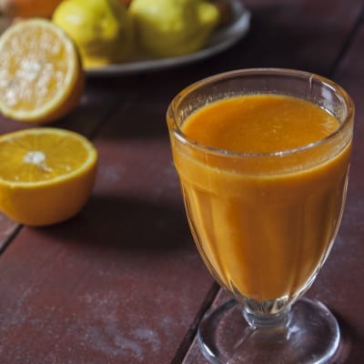 Succo di arancia, carota e limone servito in un calice con agrumi tagliati sullo sfondo