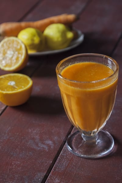 Succo di arancia, carota e limone servito in un calice con agrumi tagliati sullo sfondo