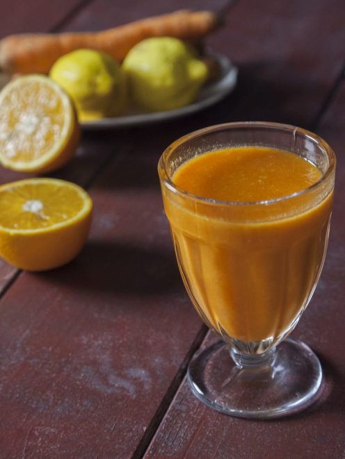 Succo di arancia, carota e limone servito in un calice con agrumi tagliati sullo sfondo