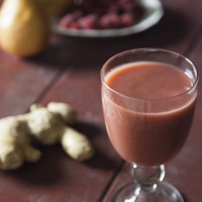Succo di pera, lamponi e zenzero servito con radice di zenzero fresca e lamponi sullo sfondo