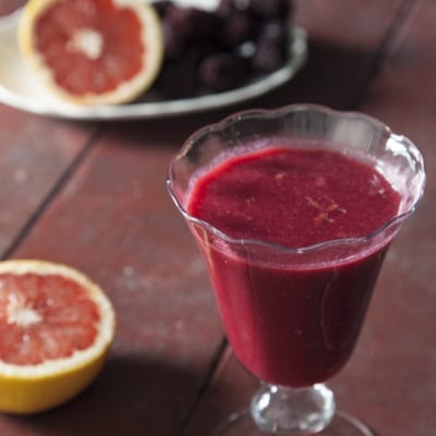 Succo di pompelmo rosa, ribes e more servito in calice con mezzi pompelmi accanto