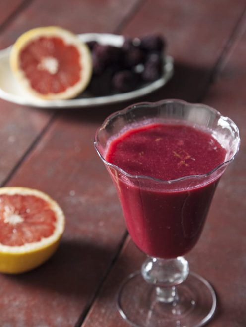 Succo di pompelmo rosa, ribes e more servito in calice con mezzi pompelmi accanto