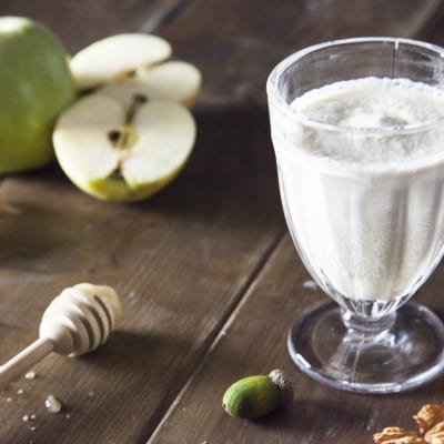 Smoothie di mela, miele e cannella servito in calice con mele verdi tagliate sullo sfondo