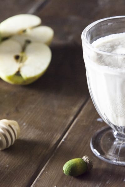 Smoothie di mela, miele e cannella servito in calice con mele verdi tagliate sullo sfondo