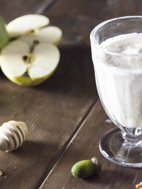 Smoothie di mela, miele e cannella servito in calice con mele verdi tagliate sullo sfondo