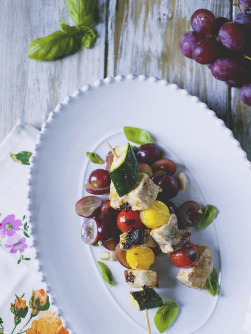 Souvlaki di pesce spada con zucchine, pomodorini e uva, guarnito con foglie di basilico