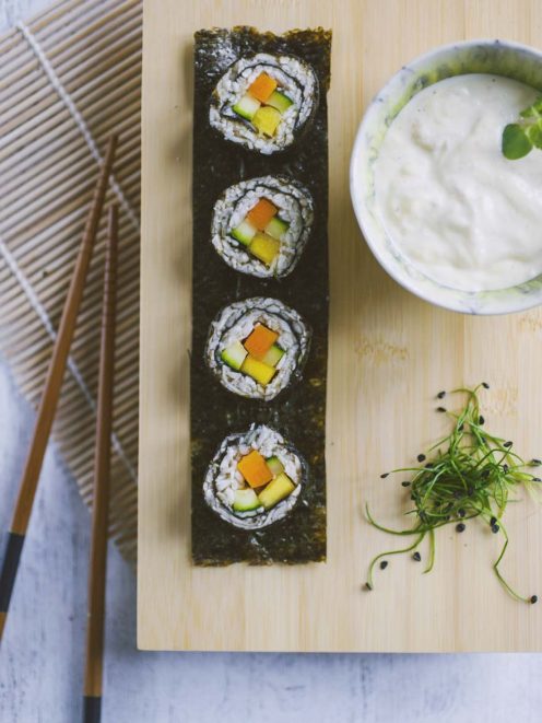 Sushi di verdure con carota, zucchina e mango avvolti in alga nori, serviti con salsa cremosa