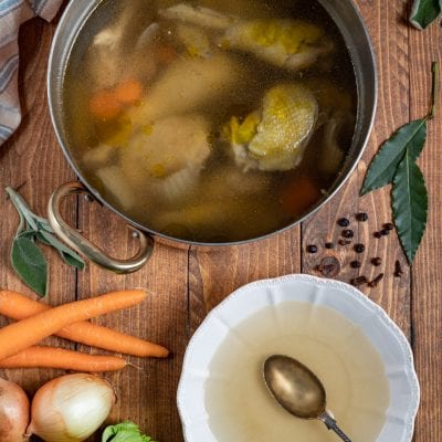 Brodo di cappone in cottura con carote e verdure, servito in una fondina con cucchiaio