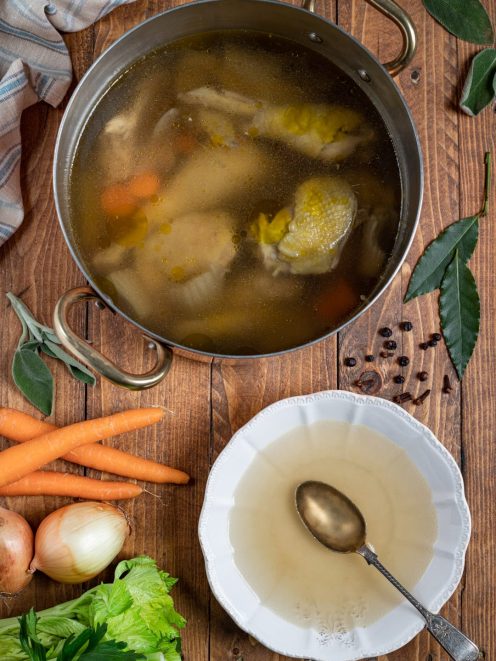 Brodo di cappone in cottura con carote e verdure, servito in una fondina con cucchiaio