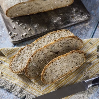 Pane al farro affettato con mollica alveolata e semi di girasole, accanto alla pagnotta intera