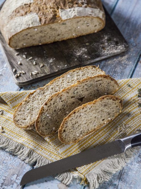 Pane al farro affettato con mollica alveolata e semi di girasole, accanto alla pagnotta intera