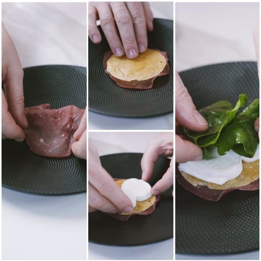 Mani che compongono la millefoglie di bresaola con cialdina di formaggio, mozzarella e spinaci freschi