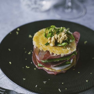 Millefoglie di bresaola a strati con mozzarella, rucola e noci, guarnita con scaglie di grana