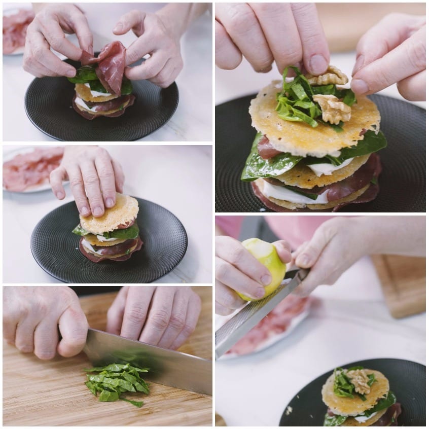 Mani che assemblano una millefoglie salata a strati con bresaola, cialdine, mozzarella e spinaci