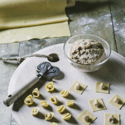 Tortellini alla bolognese in preparazione: sfoglia fresca, ripieno e tortellini già formati su asse infarinato